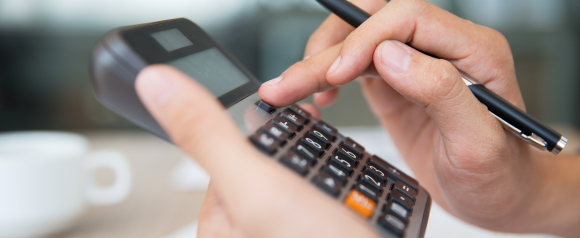 Close-up of a person using a black calculator with one hand while holding a black pen in the other. The image suggests focus and precision, possibly related to preparing community tax assessments or financial documents.