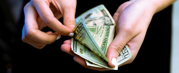 A person holds and counts several U.S. twenty-dollar bills with neatly manicured hands. The image highlights personal cash flow and financial control, echoing the support services offered by Accredited Debt Relief.
