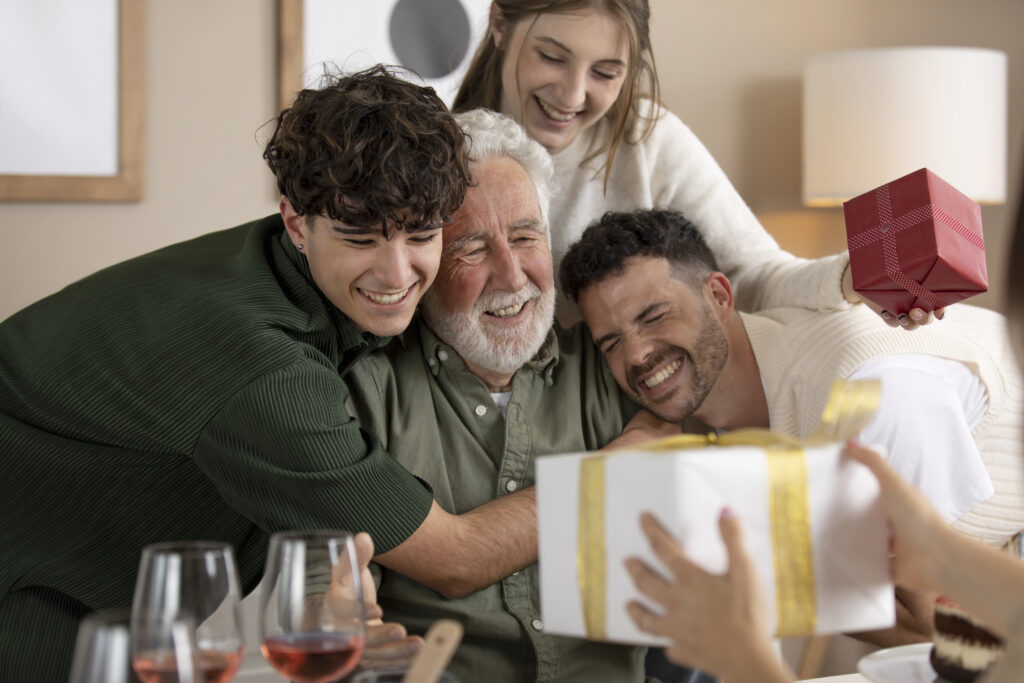 Smiling senior father receiving Christmas gifts from adult children at home.