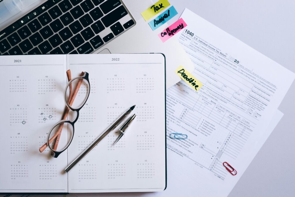A flat lay of tax preparation items including a laptop keyboard, a 2021–2022 calendar planner with eyeglasses and pens, and a 1040 U.S. Individual Income Tax Return form marked with sticky notes labeled “Tax,” “Annual,” “Company,” and “Deadline.” The image visually represents planning and documentation for IRS audits or tax relief.