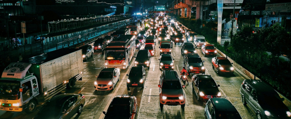 Nighttime view of heavy urban traffic with cars, buses, motorcycles, and a delivery truck filling multiple lanes on a city highway. The image conveys the complexity of fleet tracking in congested conditions, aligning with Teletrac Navman's focus on efficient vehicle monitoring.