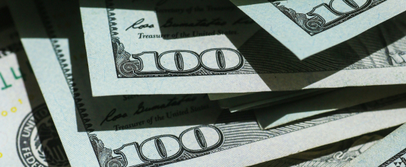 Close-up image of multiple overlapping U.S. one hundred dollar bills, highlighting the number 