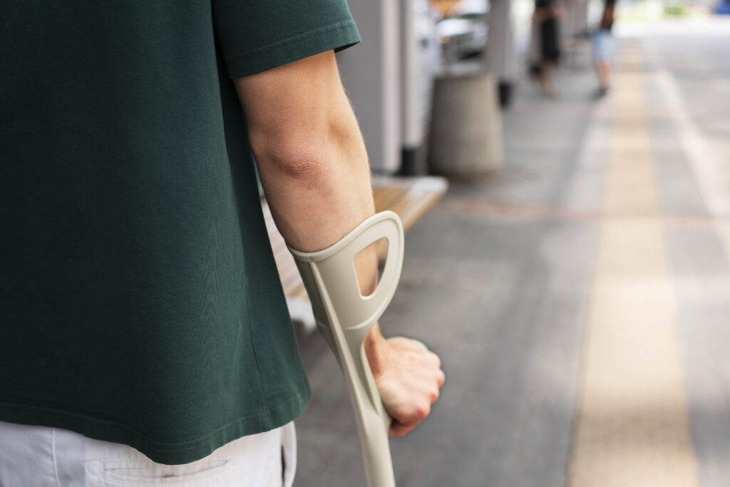 Close-up of an injured person using a crutch on a city sidewalk, illustrating the recovery process often covered by a personal injury settlement.