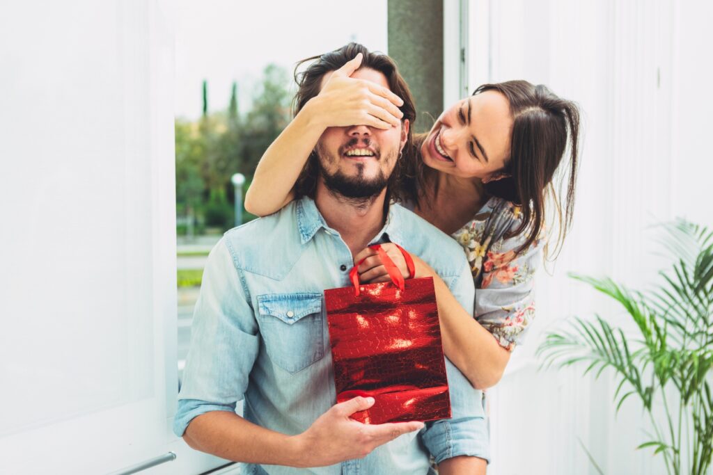 Smiling woman covering her boyfriend's eyes to surprise him with his first Valentine gift