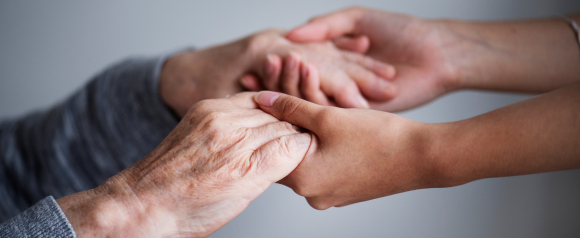 Close-up of a younger person gently holding the hands of an elderly individual, highlighting care, trust, and emotional support. The image suggests the importance of reliable medical alert systems like ADT for aging loved ones' safety and peace of mind.