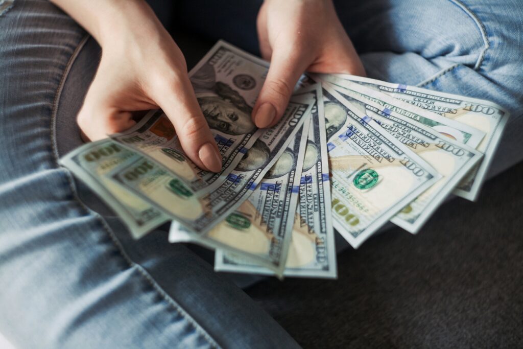 Hands holding a large fan of one hundred dollar bills, symbolizing the unclaimed refund money you lose if you don't know what happens if you don't file your taxes but don't owe anything.