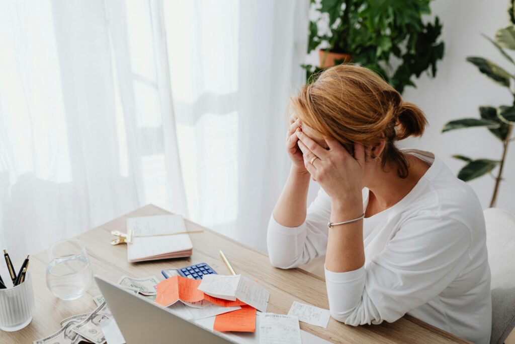 A stressed woman with hands over her face sitting at a desk overwhelmed by receipts, bills, and financial papers, illustrating the anxiety of receiving an IRS CP504 notice.