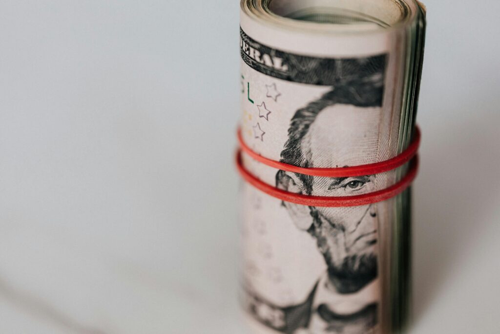 Roll of US dollar bills secured with a red rubber band against a light background, symbolizing accumulated debt and financial pressure. The image represents the search for legitimate debt relief programs and highlights the importance of learning how to avoid debt relief scams when seeking financial help.
