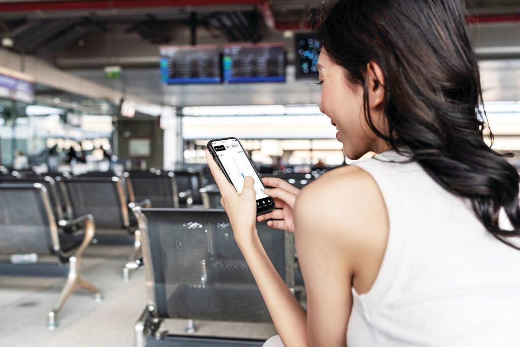 A woman in an airport lounge using a smartphone app to adjust the settings and connectivity of her Sennheiser hearing aids.