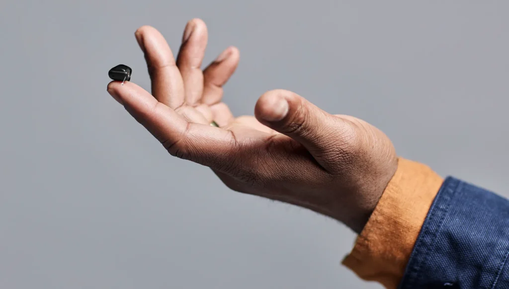 Alt text:Signia Insio Charge&Go CIC IX hearing aid resting on a person's fingertip, showing its compact completely-in-canal size