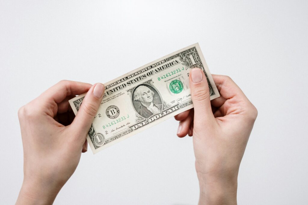 Hands holding a one dollar bill against a plain background, symbolizing financial relief and reduced debt payments. The image represents potential savings through debt forgiveness or debt settlement programs.