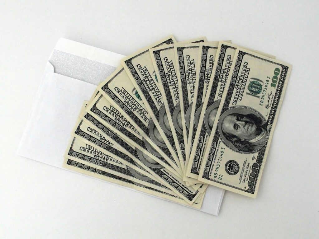 Alt text: Fan of hundred dollar bills coming out of an envelope representing an IRS tax refund