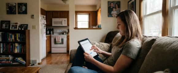 Woman sitting on a couch at home filling out a personal loan application on a tablet near a sunny window