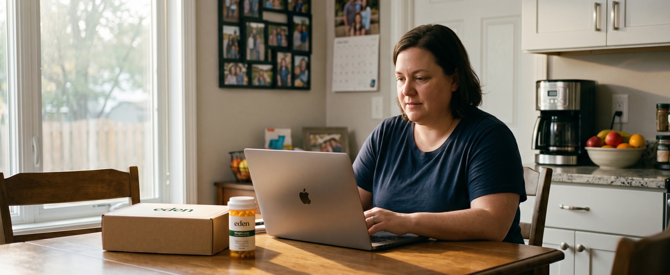 Woman with higher BMI using a laptop at a kitchen table with an Eden weight loss medication delivery box and prescription bottle nearby