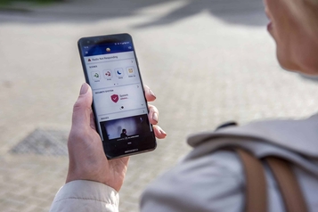 Person holding a smartphone showing the ADT home security app with arming status and a live camera feed.