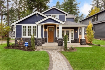 Two-story navy Craftsman home with a Brinks Home Security yard sign by the front walkway.