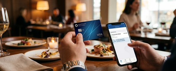Diner's hands holding a blue Chase Sapphire Preferred Visa Signature credit card and a smartphone showing a $112.50 restaurant transaction with 3x dining points earned, at an upscale restaurant table with plated food, wine glasses, and candlelight