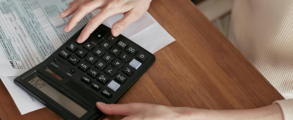 A person using a calculator while reviewing a U.S. 1040 tax form on a wooden desk, representing financial planning or debt calculations. This image could relate to JG Wentworth debt relief services aimed at helping individuals manage or resolve their tax burdens.