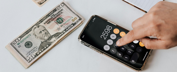 Person using a smartphone calculator showing 2598, surrounded by stacks of U.S. dollar bills, representing financial planning or debt relief, as offered by Cambridge Credit Counseling.