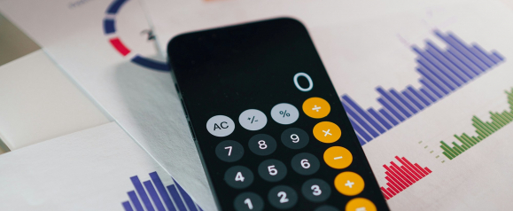 A smartphone with a calculator app open lies on top of colorful financial charts featuring red, green, and blue bar graphs. The setup conveys data analysis and budgeting, aligning with the debt relief services offered by DebtBlue.