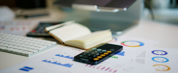 A modern workspace with a smartphone calculator app, financial graphs, an open notebook, and a keyboard arranged neatly on a desk. The image represents strategic financial planning and organization, key values associated with Steadywise.
