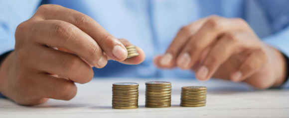 A person in a blue shirt stacks coins into neat piles on a white table, focusing on organizing finances. The image reflects budgeting and financial planning, core themes associated with United Settlement’s debt relief services.