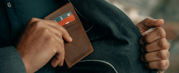 A person places a slim brown wallet holding credit cards into the inner pocket of a dark blazer. The image suggests financial responsibility and credit management, aligning with Cero Deuda’s mission of helping clients reduce debt.