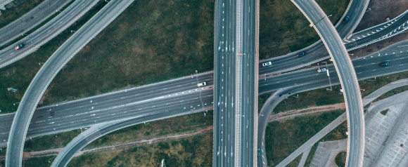 Aerial view of a multi-level highway interchange with several vehicles traveling in different directions. The image highlights traffic flow and road complexity, ideal for illustrating vehicle tracking or GPS navigation systems like OneStep GPS.