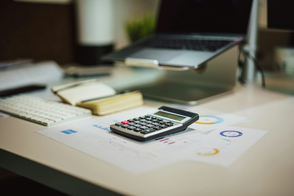 A calculator resting on printed financial charts beside a keyboard and open notebook on a modern desk setup. The workspace suggests financial planning or tax preparation, relevant to topics like the Annual Gift Tax Exclusion 2026.