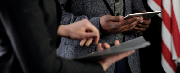 Close-up of two professionals using tablets during a legal proceeding or briefing, with an American flag visible in the background. The image supports themes of modern legal practice and professionalism, reinforcing the role of Morgan and Morgan lawyers.