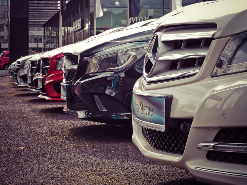 Close-up view of a row of Mercedes-Benz cars parked outside a dealership, focusing on the front grilles and license plates. These vehicles may include integrated tracking devices for security and fleet management.