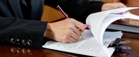 A person in a black blazer reviews and marks up a printed legal document with a gold-tipped pen, flipping through pages clipped together on a wooden desk. The image conveys the professional and thorough tax help provided by Five Star Tax Resolution.