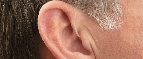 Close-up of an older man's ear with a nearly invisible MDHearing aid, featuring a thin, clear tube that blends with the skin. The image emphasizes the discreet and lightweight design of MDHearing hearing aids.