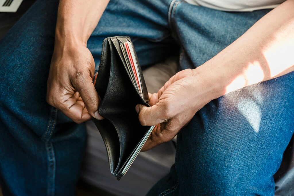 Close-up of a person in jeans sitting down and holding an open, empty black wallet, with several cards visible in the side slots. The image conveys financial stress, tying into discussions around debt consolidation versus debt settlement options.