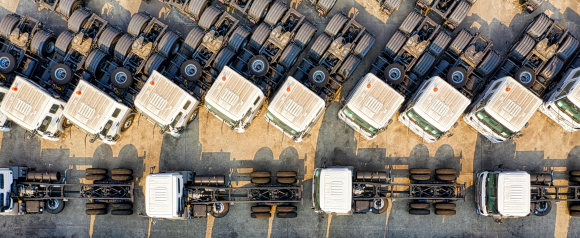 Aerial view of multiple white semi-truck cabs neatly parked in rows on a concrete lot, showcasing a large fleet from above. The organized layout emphasizes vehicle uniformity and scale, relevant to Linxup’s fleet tracking and management solutions.