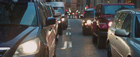 Close-up view of cars in heavy traffic on a city street at dusk, with headlights on and buildings reflected on vehicle surfaces. The image emphasizes urban congestion, ideal for illustrating real-time vehicle tracking solutions or fleet monitoring by companies like Digital Matter.