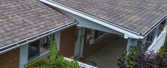 A close-up view of a residential home's roof featuring asphalt shingles in shades of gray and brown, with white gutters and trim. The image showcases the quality roofing work typical of Erie Home, emphasizing durability and curb appeal.