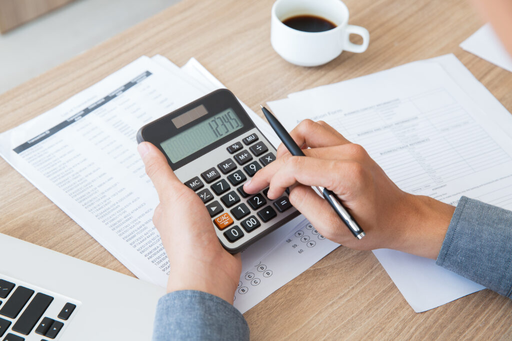 Close-up of hands using a calculator to review financial documents and avoid common tax mistakes.