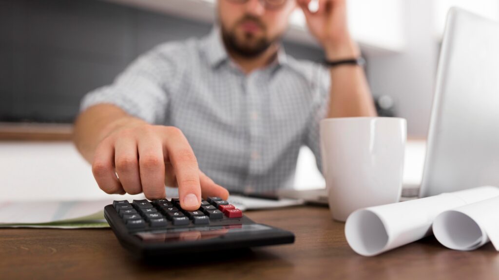 Close up of a man using a calculator to analyze finances and determine how do you qualify for tax forgiveness.