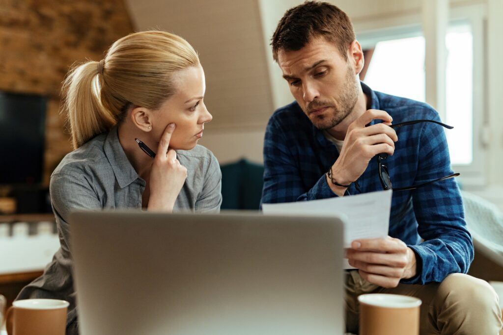 A worried couple reviewing IRS tax documents together on a couch, illustrating the need for innocent spouse relief due to hidden tax debt.