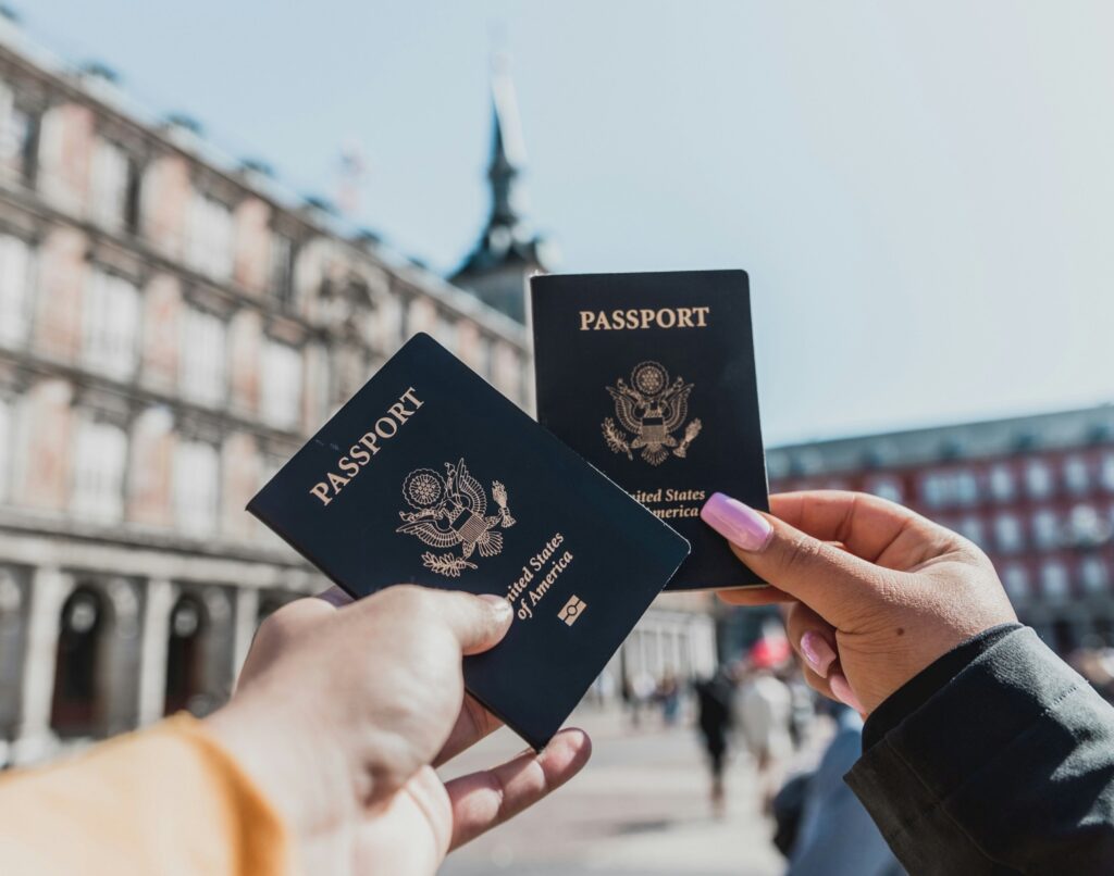 Two hands holding United States passports against a sunny European plaza background, illustrating the travel freedom lost during an IRS passport revocation for unpaid taxes.