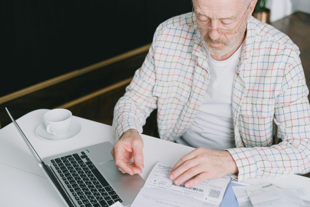 Worried senior man sitting at a desk with a laptop, reviewing a paper tax document and concerned about whether the IRS can garnish Social Security benefits.