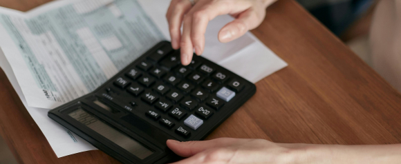 Hands using a large black calculator next to IRS Form 1040 on a wooden table. The image represents tax preparation and financial calculations, supporting the concept of tax relief services offered by Civic Tax Relief.