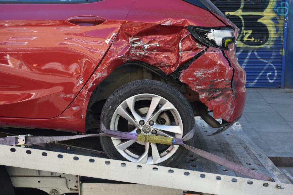 Close-up of a red car with severe rear side damage secured on a tow truck, illustrating the complex property damage claims handled by motor vehicle accident lawyers