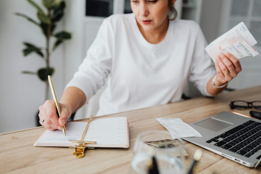 Woman holding receipts and writing in a planner to calculate her budget before enrolling in a debt management program.