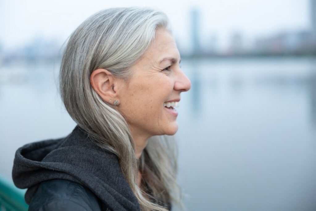 Side profile of a smiling woman wearing a discreet Audicus hearing aid, demonstrating the behind-the-ear fit for Audicus reviews