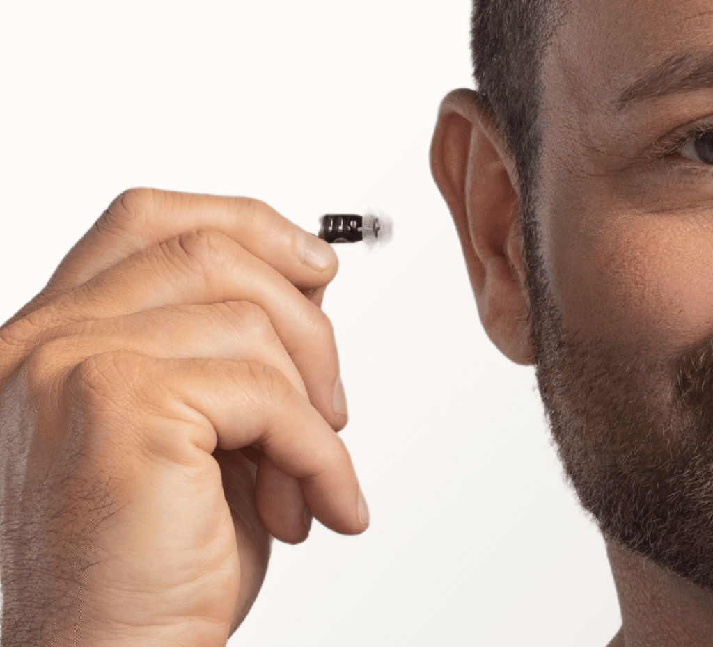 Close-up of a man's hand inserting a tiny, black Eargo in-the-canal hearing aid into his ear.