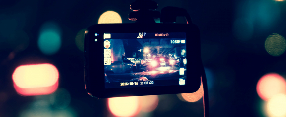 Close-up of a dashcam-style device mounted inside a vehicle, recording night traffic in 1080p HD with visible on-screen date and timestamp. The blurred city lights in the background highlight real-time fleet tracking in action, illustrating GPS Insight technology in use.