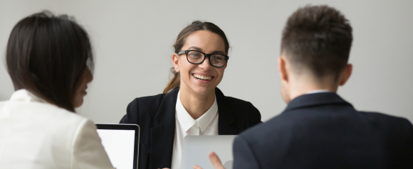 Smiling HR professional in glasses leads a meeting with two colleagues across a desk, creating a welcoming and collaborative office atmosphere. The team sits with open laptops, suggesting a productive discussion powered by HiBob HR software to support people management and workplace engagement.