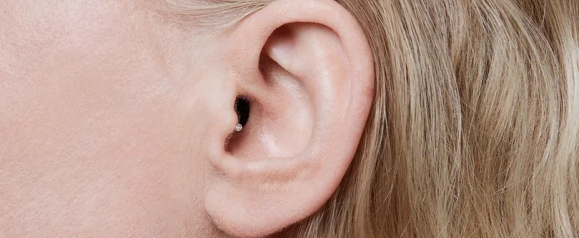 Close up of a person’s ear wearing a small in ear hearing aid that fits discreetly inside the ear canal. The nearly invisible design highlights how Oticon hearing aids provide subtle and effective hearing support for everyday conversations.